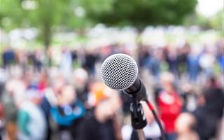 forground shows microphone outdoors at rally people blurred in background